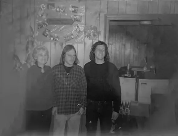 Three individuals stand in a cozy room featuring a fireplace, discussing roofing options in a warm, inviting atmosphere.
