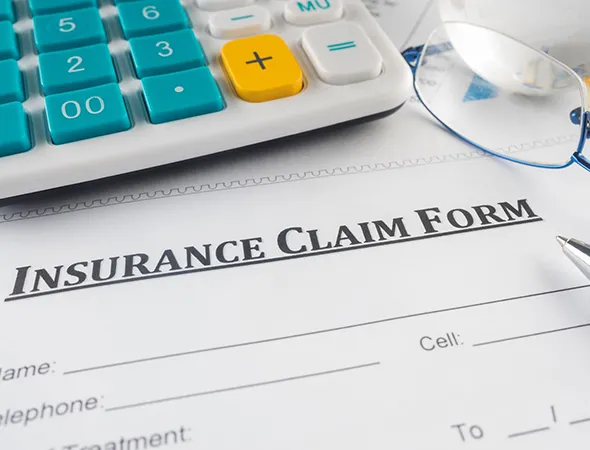 Insurance claim form alongside glasses and a calculator, indicating a focus on roofing-related financial assessments.