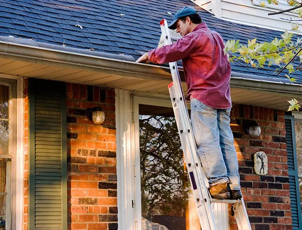 A man on a ladder performs roofing work on a house, focusing on repairs and maintenance of the upper structure.
