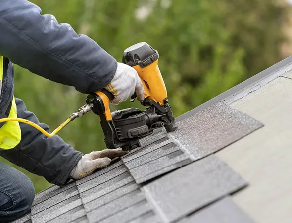 A man skillfully operates a nail gun to secure a roofing shingle in place on a residential structure.