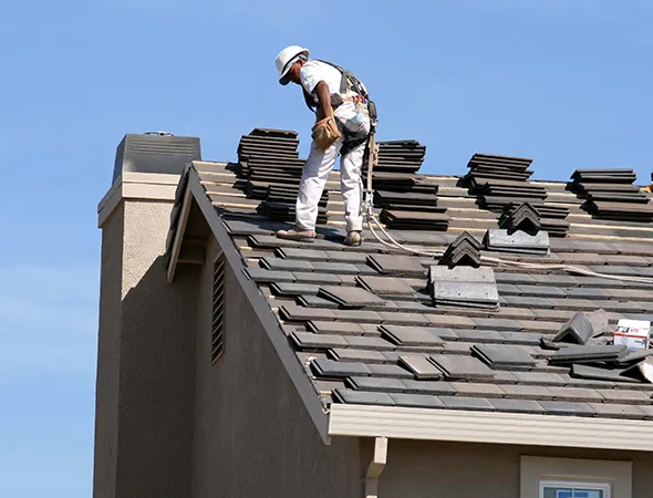 A man stands on a house roof, using a tool for roofing work, focused on repairing or installing shingles.