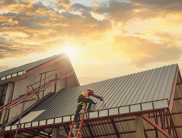 A man is positioned on a roof next to a ladder, actively involved in roofing tasks, demonstrating skill and focus.